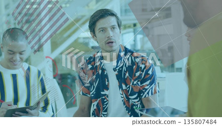 Speaking male worker wearing patterned shirt in modern workspace, with tablet laptop monitors 135807484