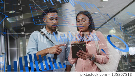 Business-clad professionals analyzing data in airport hall with tablet device and floating charts Business-clad professionals analyzing data in airport hall with tablet device and floating charts 135807518