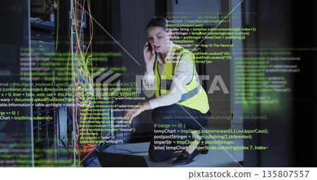 Kneeling IT tech in hi-vis vest configuring network cables in server room with smartphone, laptop Kneeling IT tech in hi-vis vest configuring network cables in server room with smartphone, laptop 135807557