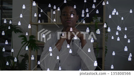 Reviewing digital network overlay at office desk by doctor wearing lab coat and stethoscope 135808566