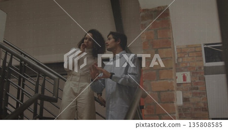 Standing coworkers discussing metal staircase handrail by brick pillar fire safety sign, copy space Standing coworkers discussing metal staircase handrail by brick pillar fire safety sign, copy space 135808585