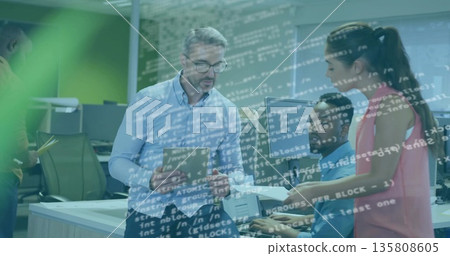 Managing team lead holding tablet guiding developers typing at tech office desk, with code overlay 135808605