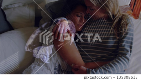 Embracing couple leaning into each other on bed in softly lit bedroom, with world map projection Embracing couple leaning into each other on bed in softly lit bedroom, with world map projection 135808615