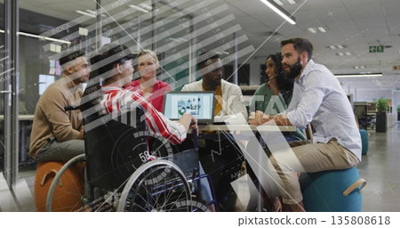Coworkers collaborating around round table in open-plan office, with laptop charts and wheelchair 135808618