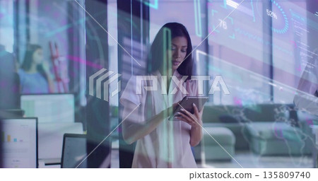 Holding tablet businesswoman analyzing data behind glass partition at office with digital overlays Holding tablet businesswoman analyzing data behind glass partition at office with digital overlays 135809740