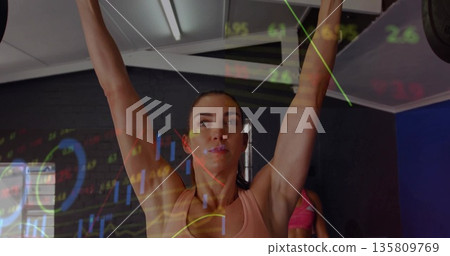 Mid adult lifter in pink sportswear lifting barbell overhead in gym, with graph overlays 135809769