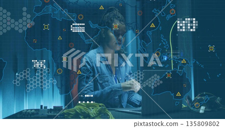Monitoring engineer wearing denim shirt operating laptop at tech lab, with cables and digital map 135809802