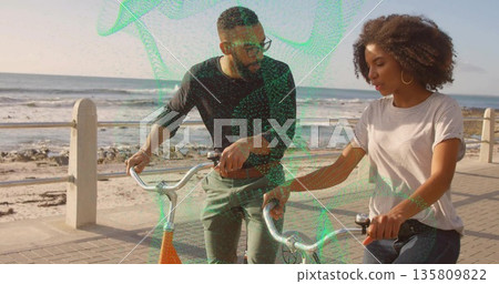 Walking side by side, friends holding bicycles on seaside promenade by railing and posts, chatting 135809822