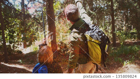Looking up father and son in gear holding walking poles in forest with yellow-black hiking backpack 135809824