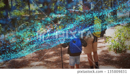 Pointing father guiding son holding hiking stick on pine forest trail wearing backpacks, copy space Pointing father guiding son holding hiking stick on pine forest trail wearing backpacks, copy space 135809831