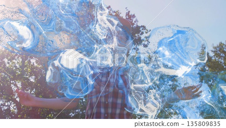 Woman wearing sleeveless plaid shirt creating shimmering soap bubbles in park, with bubble wand 135809835