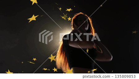 Woman being backlit and wearing crop-top in studio, featuring gold star confetti on dark backdrop 135809853