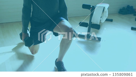 Performing weighted lunge man in athletic shirt and shorts by home gym bench with hex dumbbells Performing weighted lunge man in athletic shirt and shorts by home gym bench with hex dumbbells 135809861
