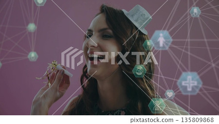 Partygoer wearing novelty hat blowing party horn in pink studio, floating confetti and hex symbols 135809868