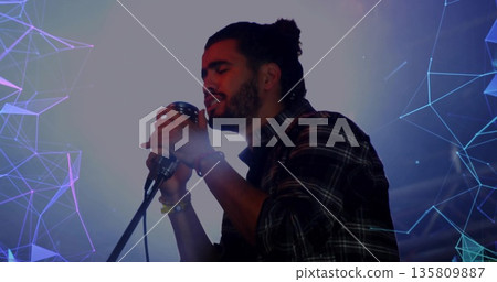 Performing singer in flannel shirt gripping vintage mic on stand on stage, purple blue projections 135809887