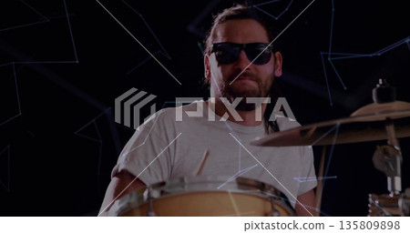 Male drummer wearing sunglasses hitting drum kit in studio, with constellation patterns Male drummer wearing sunglasses hitting drum kit in studio, with constellation patterns 135809898