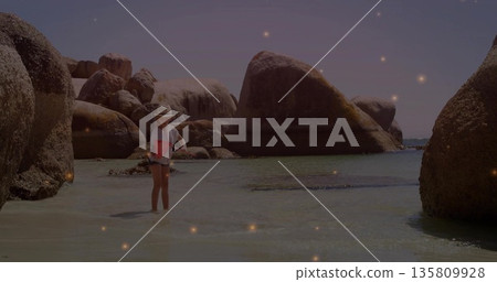Wading child wearing straw hat, striped shirt, denim shorts in rocky cove by sea, copy space 135809928