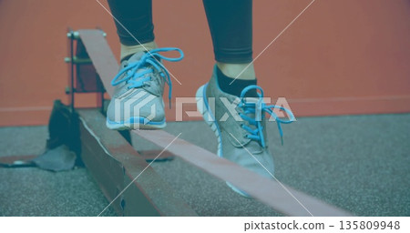 Balancing woman's legs and feet wobbling on slackline at fitness studio, with blue-laced sneakers 135809948