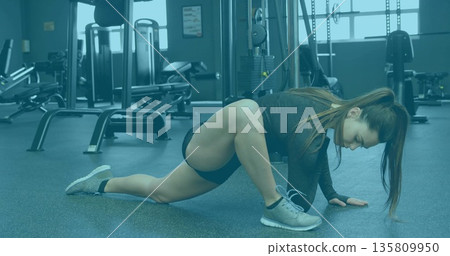 Athlete stretching in gym wearing black workout clothes, with weight benches cable pulley station Athlete stretching in gym wearing black workout clothes, with weight benches cable pulley station 135809950
