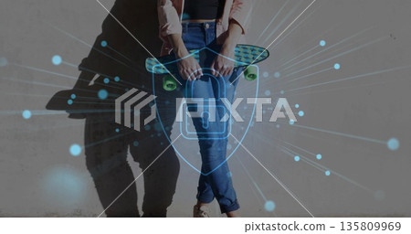 Leaning woman holding skateboard against concrete wall displaying digital shield with padlock nodes 135809969