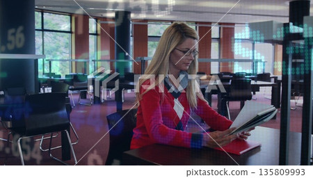 Woman wearing glasses and sweater reviewing binder in library with red folder, financial overlay Woman wearing glasses and sweater reviewing binder in library with red folder, financial overlay 135809993