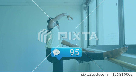 Stretching woman extending right leg on barre while lifting left arm in studio, windows, heater Stretching woman extending right leg on barre while lifting left arm in studio, windows, heater 135810005