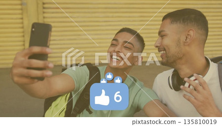 Smiling friends capturing selfie at yellow shutter with smartphone headphones like-count overlay 135810019