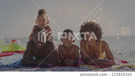 Lying family in swimwear smiling on striped towels at shoreline, with swim ring and beach ball Lying family in swimwear smiling on striped towels at shoreline, with swim ring and beach ball 135810103