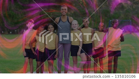 Smiling soccer coach and youth team gathering on grassy field, with soccer ball and goal frame 135810106