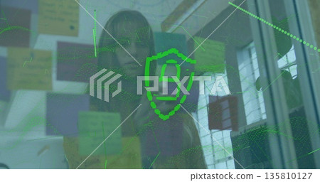 Aligning woman in purple top viewing digital shield on glass partition at office, with sticky notes 135810127