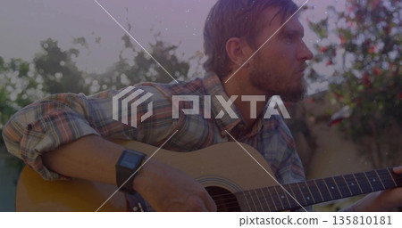 Playing musician wearing plaid shirt strumming acoustic guitar in garden at sunset, with smartwatch 135810181