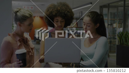 Collaborating trio of women analyzing data on laptop in open-plan office with disposable coffee cup 135810212