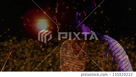 Performing musician wearing striped shirt singing into mic in studio, spotlight and golden bokeh Performing musician wearing striped shirt singing into mic in studio, spotlight and golden bokeh 135810222