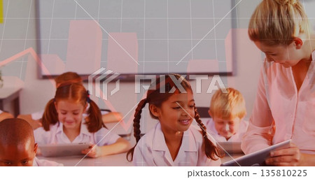 Leaning teacher guiding girl tapping tablet at student desk in classroom, with interactive display 135810225