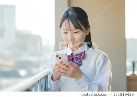 放學後,一名國中女生正在操作智慧型手機 放學後,一名國中女生正在操作智慧型手機 135810429