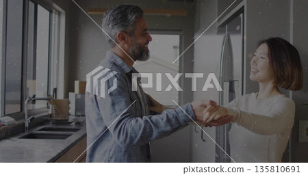 Dancing mature couple holding hands in modern home kitchen, with stainless steel refrigerator Dancing mature couple holding hands in modern home kitchen, with stainless steel refrigerator 135810691