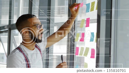 Man in white t-shirt red suspenders placing notes on glass in meeting room, with data overlays Man in white t-shirt red suspenders placing notes on glass in meeting room, with data overlays 135810701