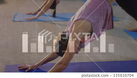 Woman in pink top and leggings holding downward dog in studio, with yoga mats, graph overlay 135810704