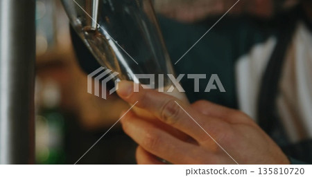 Pouring bartender hands filling tall beer glass at bar interior, with beer tap and frothy head Pouring bartender hands filling tall beer glass at bar interior, with beer tap and frothy head 135810720