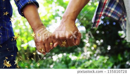 Linking senior couple in plaid shirts hooking pinkies in garden with trees, with gold wedding bands Linking senior couple in plaid shirts hooking pinkies in garden with trees, with gold wedding bands 135810728