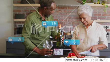 Senior couple cooking together in modern home kitchen, with wine bottle and red peppers Senior couple cooking together in modern home kitchen, with wine bottle and red peppers 135810739