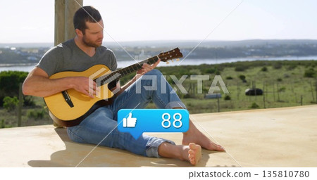 Strumming man in casual outfit on veranda by wooden post with acoustic guitar, thumbs-up icon 88 135810780