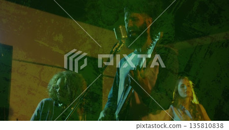 Singing bearded man strumming electric guitar on green spotlit club stage, with backing vocals 135810838