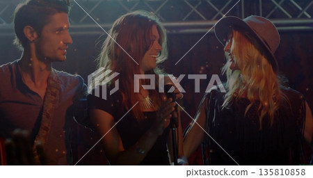 Performing bandmates smiling while playing on stage under truss with guitar and microphone stand Performing bandmates smiling while playing on stage under truss with guitar and microphone stand 135810858