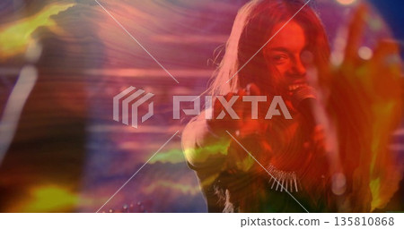 Performing singer in dark gear pointing to viewer on stage, with mic, necklace, lights, copy space Performing singer in dark gear pointing to viewer on stage, with mic, necklace, lights, copy space 135810868