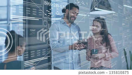 Pointing businessman in blue shirt holding smartphone at glass wall in office, with digital charts Pointing businessman in blue shirt holding smartphone at glass wall in office, with digital charts 135810875