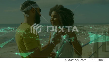 Standing couple facing each other on sandy beach with sunglasses, bandana, metal railing overlay Standing couple facing each other on sandy beach with sunglasses, bandana, metal railing overlay 135810890