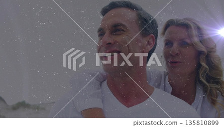 Laughing couple wearing white T-shirt and blouse posing piggyback on sandy beach, with lens flare Laughing couple wearing white T-shirt and blouse posing piggyback on sandy beach, with lens flare 135810899