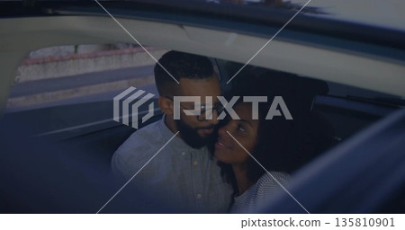 Leaning couple sharing kiss through open window of parked car beside sidewalk, with eyeglasses Leaning couple sharing kiss through open window of parked car beside sidewalk, with eyeglasses 135810901