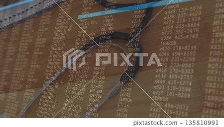 Displaying silver stethoscope resting on wooden desk workspace, featuring computer code overlay 135810991